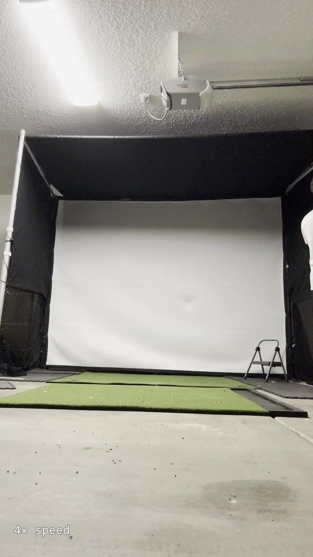 Photo of the StowGolf prototype deployed in a garage: black shell, white impact screen, hitting mat in front